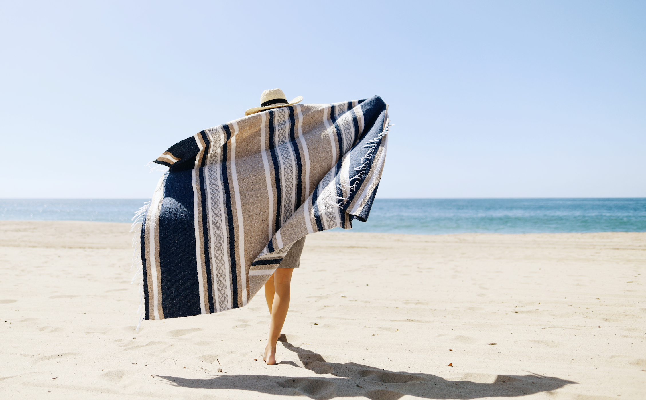 A woman walking on the beach draped in a Mexican Blanket.