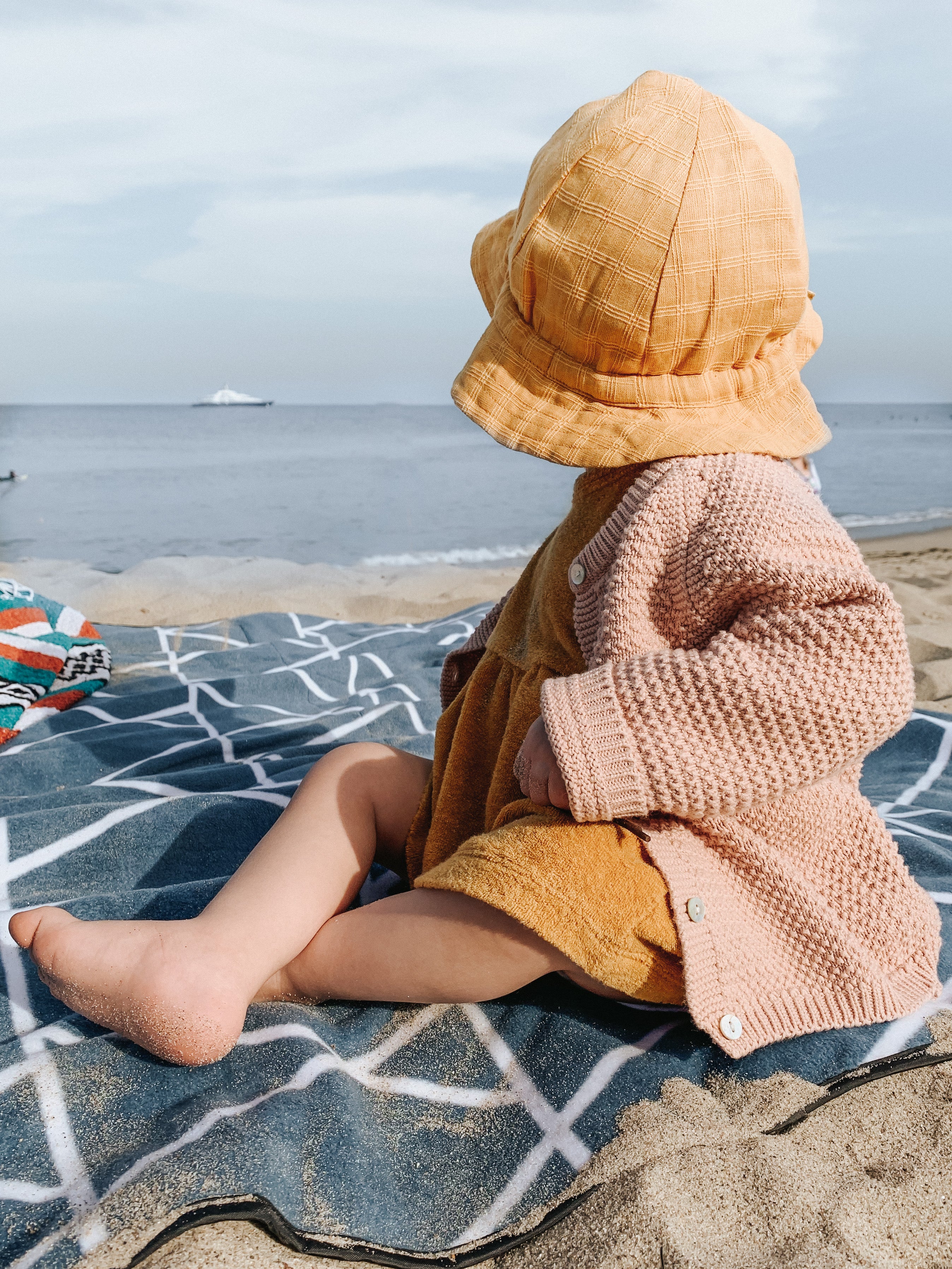 A child sitting on a picnic blanket looking at the ocean.