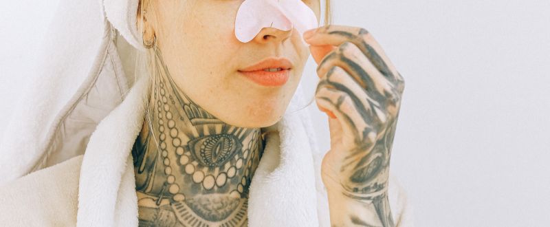 Tattooed woman in bathrobe removing nose patch