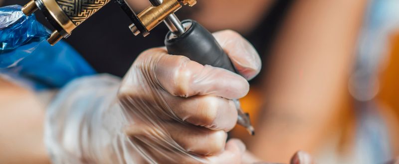 an artist tattooing a client using a tattoo gun