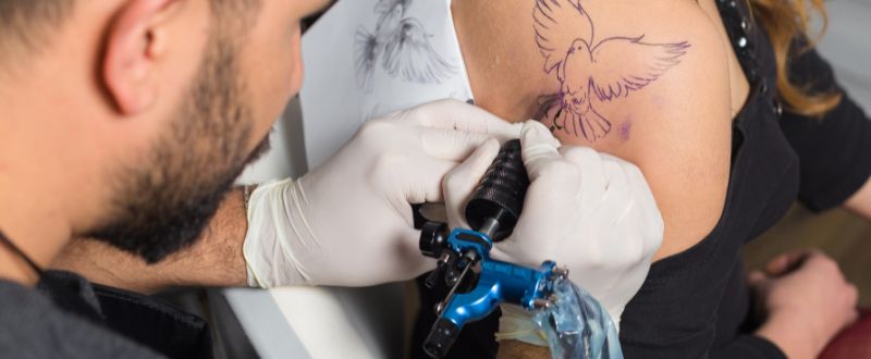 artist making an outline for bird tattoo