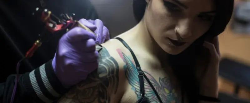 artist tattooing a woman on her shoulder