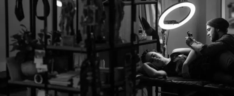 black and white picture of tattoo artist tattooing his client