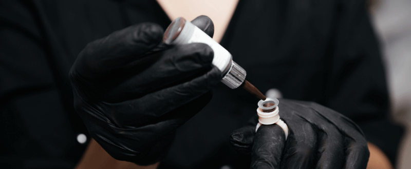 Tattoo artist pouring PMU pigment into ink cup