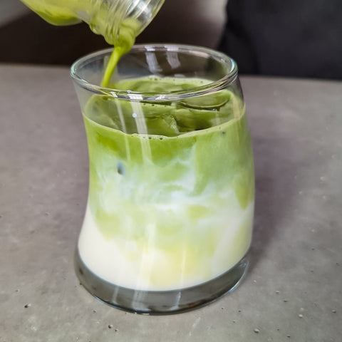 Matcha being poured into a glass of milk