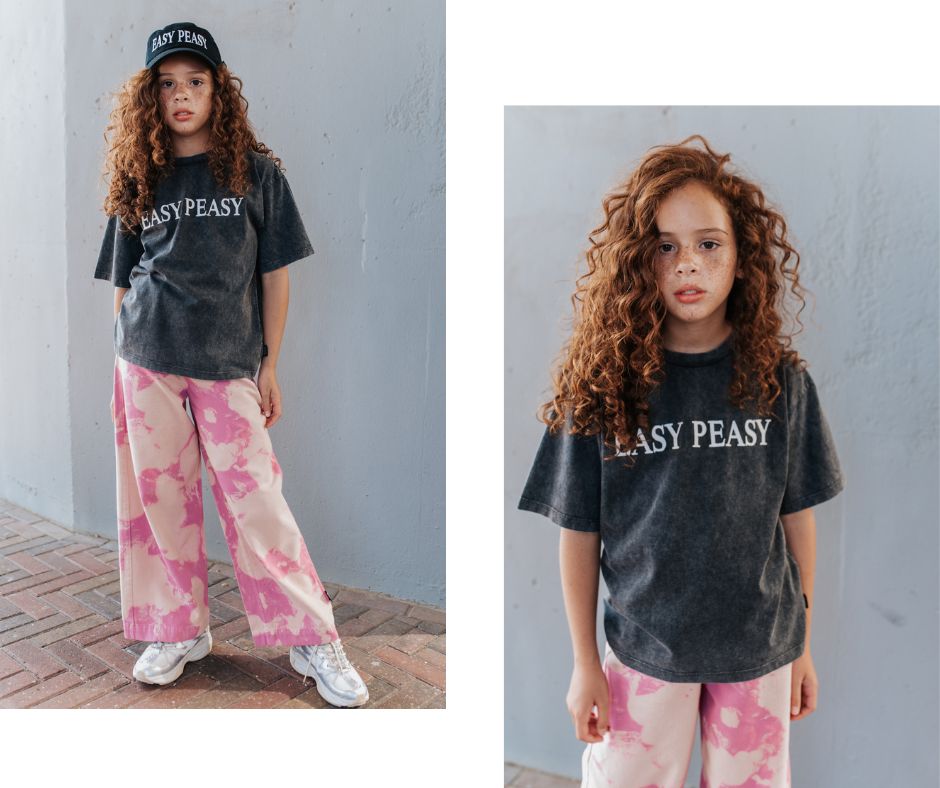 Young girl posing in Little Man Happy Easy Peasy Embroidered Skate T-Shirt and Pink Distressed Wide Leg Pants at Design Life Kids