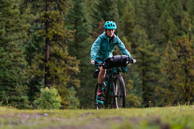Sarah Hornby riding on a trail in front of evergreen woods.