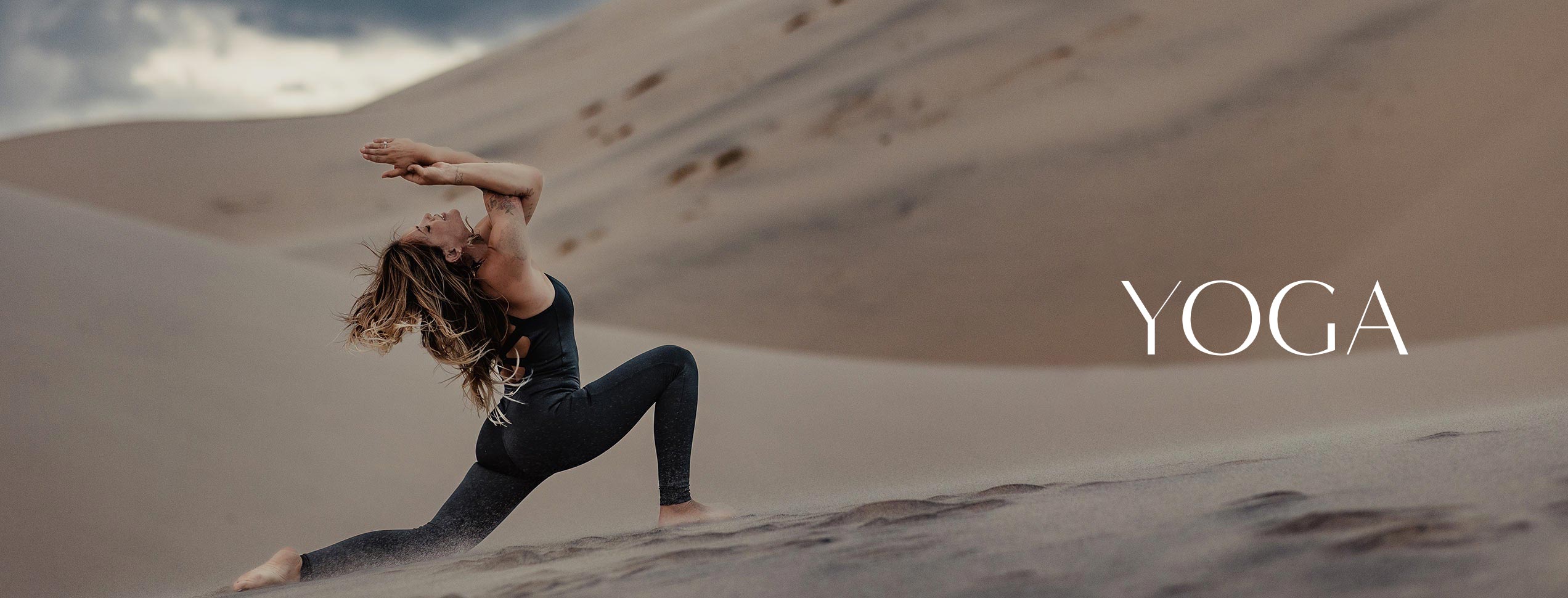 model doing yoga in a bodysuit in the middle of sand dunes