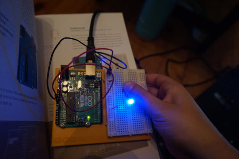 Mounted Arduino and breadboard with a series circuit set up, thumb is pressing one button to light up the blue LED