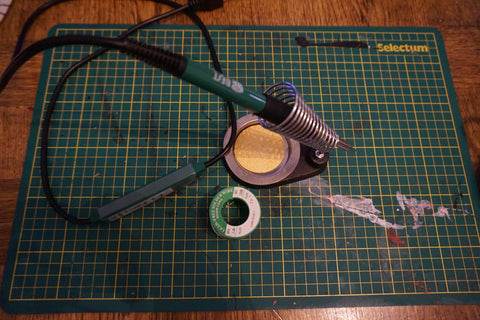 green cutting mat with a soldering iron and a spool of solder on it