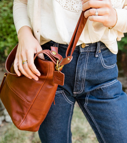 Body shot of Emily in a white blouse, dark blue jeans and a brown Osgoode Marley crossbody.