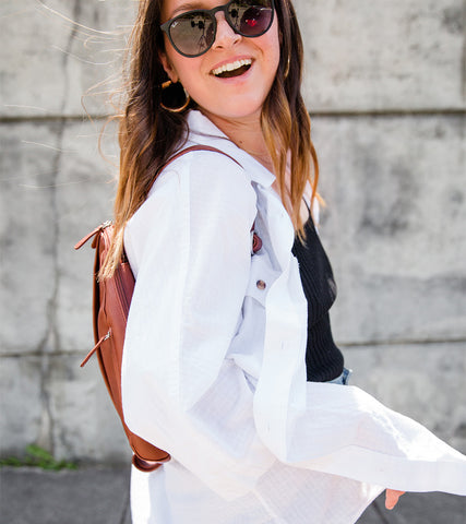 Emily in an open white button up shirt wearing sunglasses and a brown Osgoode Marley backpack.