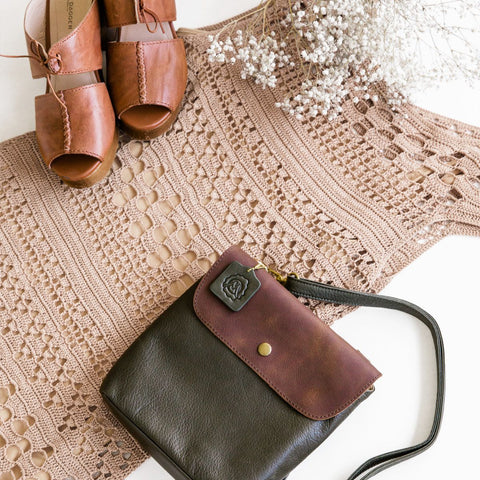 tan crochet dress frames by white flowers, tan heeled shoes and a black and brown crossbody bag on a white backdrop.