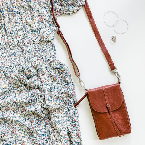blue floral dress on a white backdrop with a small, tan crossbody bag and a silver necklace.