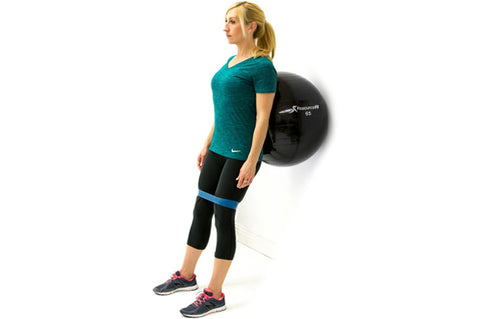 woman leaning against prosourcefit stability ball with prosourcefit loop resistance band around knees