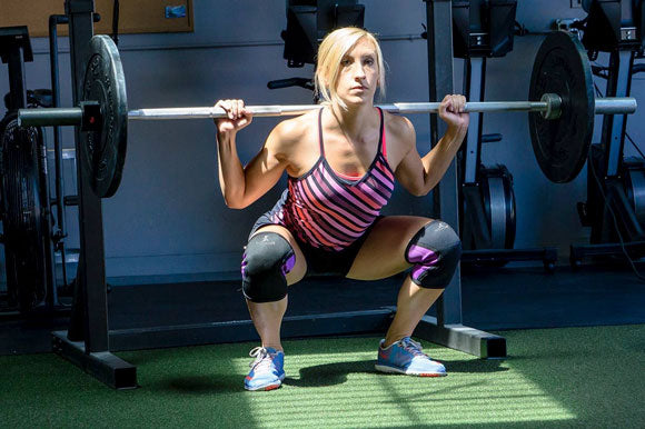 Fit woman using Woman using ProsourceFit barbell, bumper plates and knee sleeves while in a barbell squat