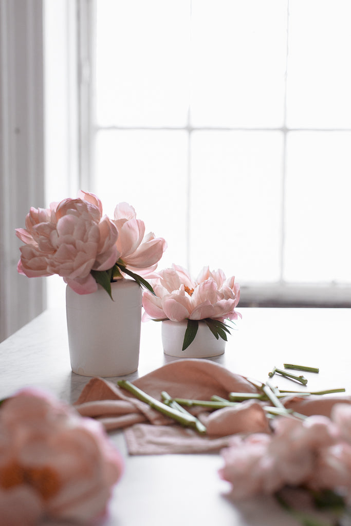 pink peonies in handmade matte white vase by a window