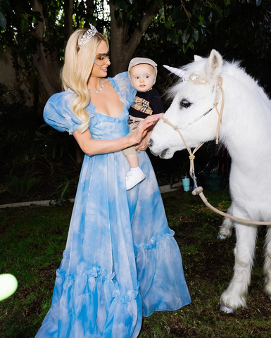 Paris Hilton wearing her BOOM style sunglasses while holding her son next to a white pony