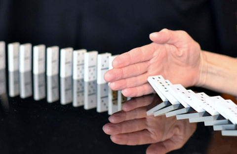 row of falling dominoes being disrupted by a hand. Denoting stopping of pain and negative thoughts