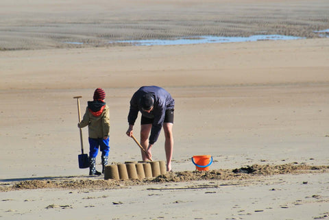 Photo of man and child on beach having fun digging in the sand