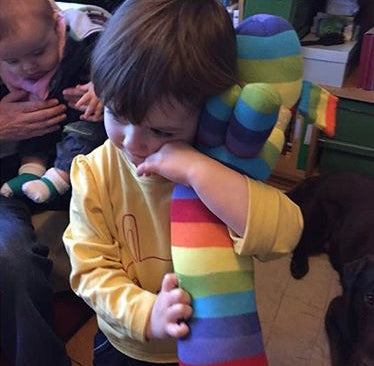 Little boy cuddling a rainbow striped Red Rufus SockDog