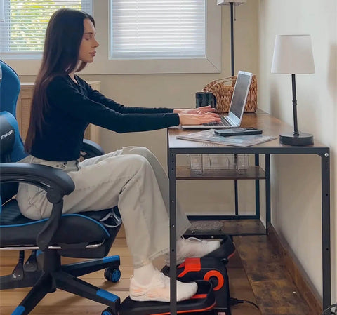 A woman sitting on her workstation and exercising with an under desk mini elliptical machine