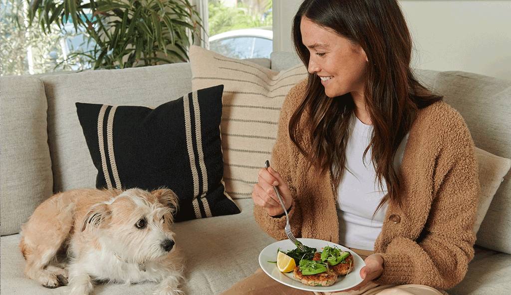 Intuitive Eating Meal - Holly happy eating turkey burgers with avocado on the couch with her dog