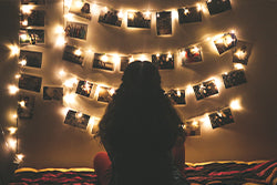 A person sitting in front of string lighting holding photographs