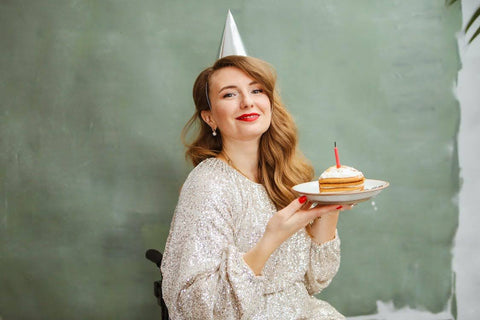 How to Make Your Resolutions Stick - Woman wearing a sparkly dress, holding a slice of cake with a candle on it