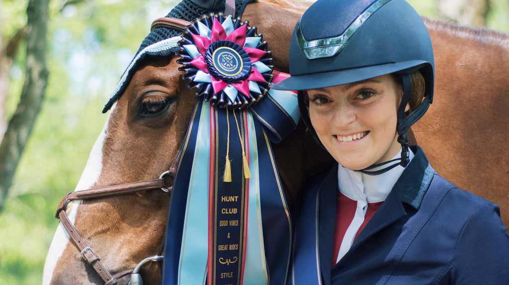 An equestrian smiles next to her horse in her competition show shirt