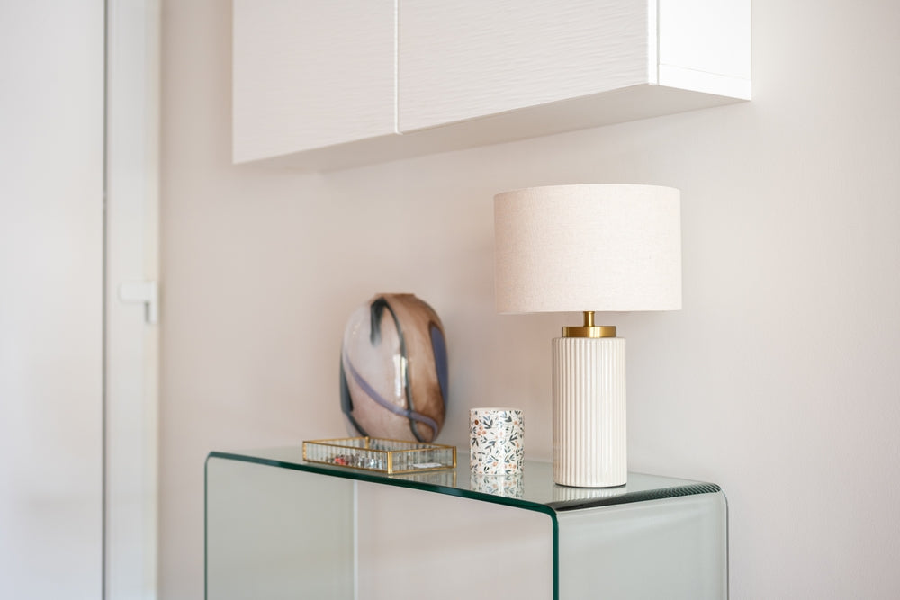 Lamp and lampshade sitting on top of a glass table in a hallway inside a home.