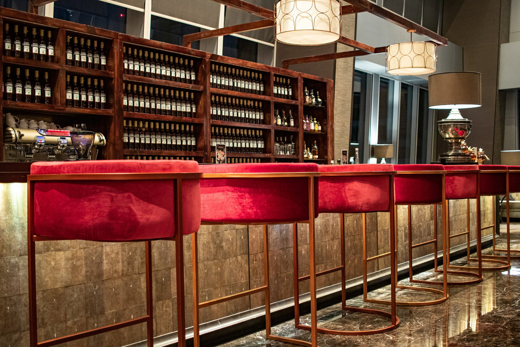 An elegant bar featuring red velvet chairs, a wine rack, and softly lit with ambient lamps.