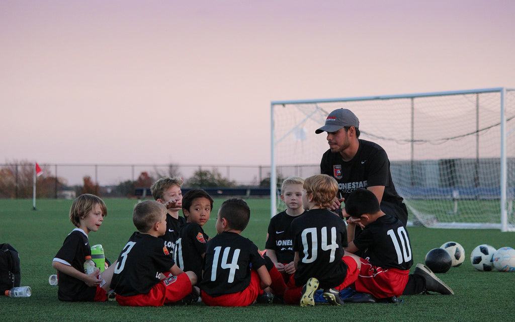 a youth soccer team sits down to rest in their after practice huddle