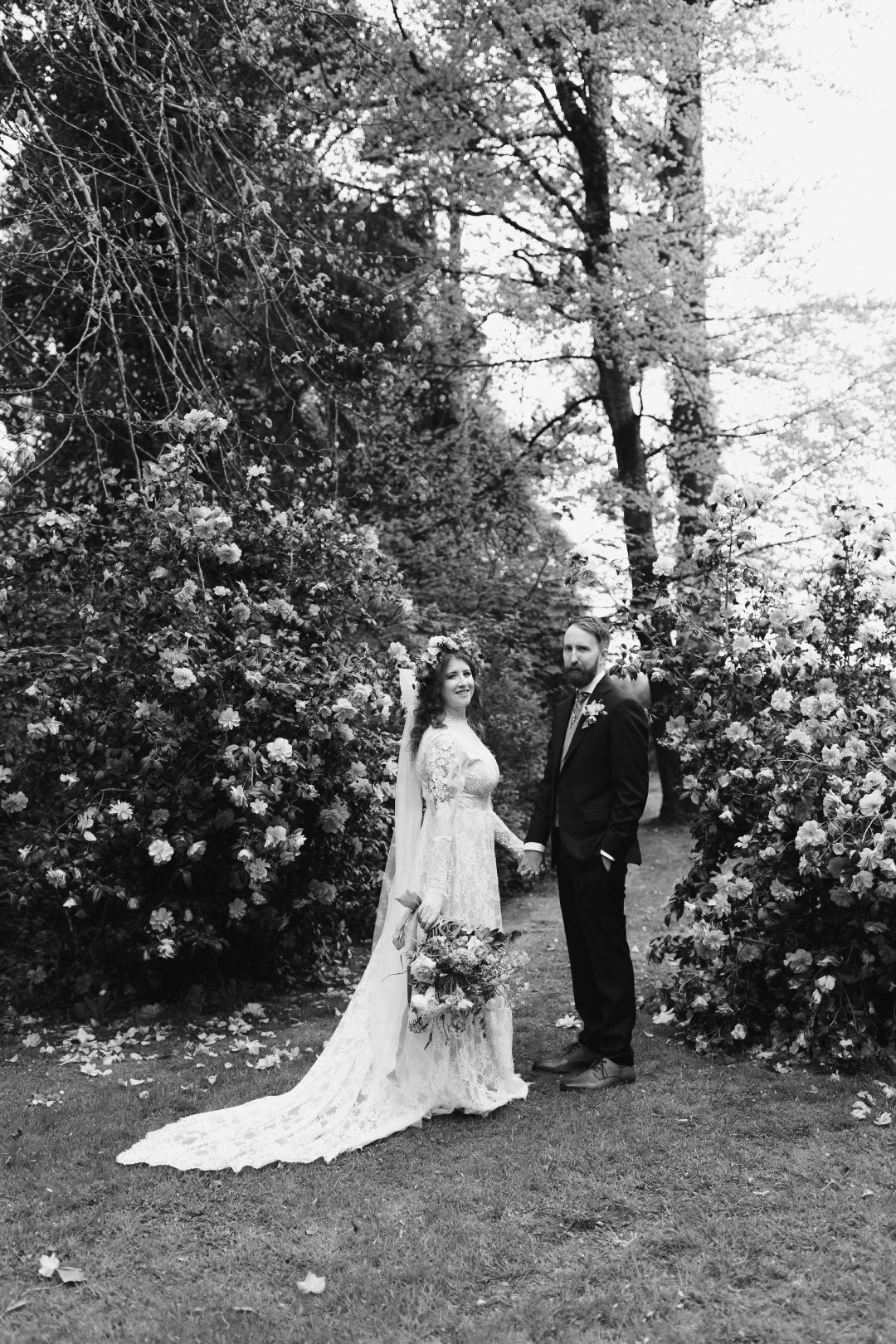 Black and white wedding photo of bride and groom walking with garden 