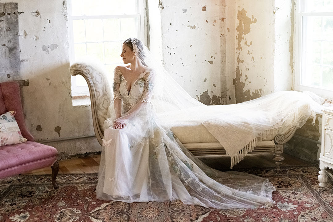 Bride seated on couch wearing wedding dress Chrysalis by Claire Pettibone