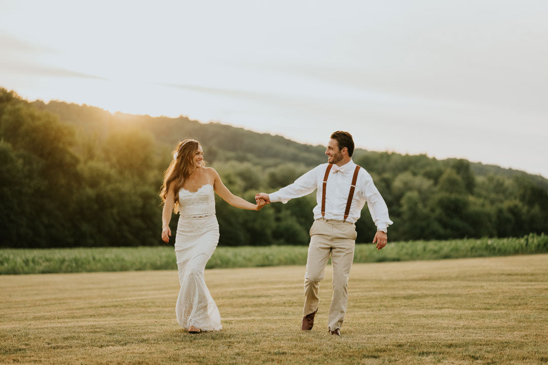 Bride and groom walking in field with a sunset