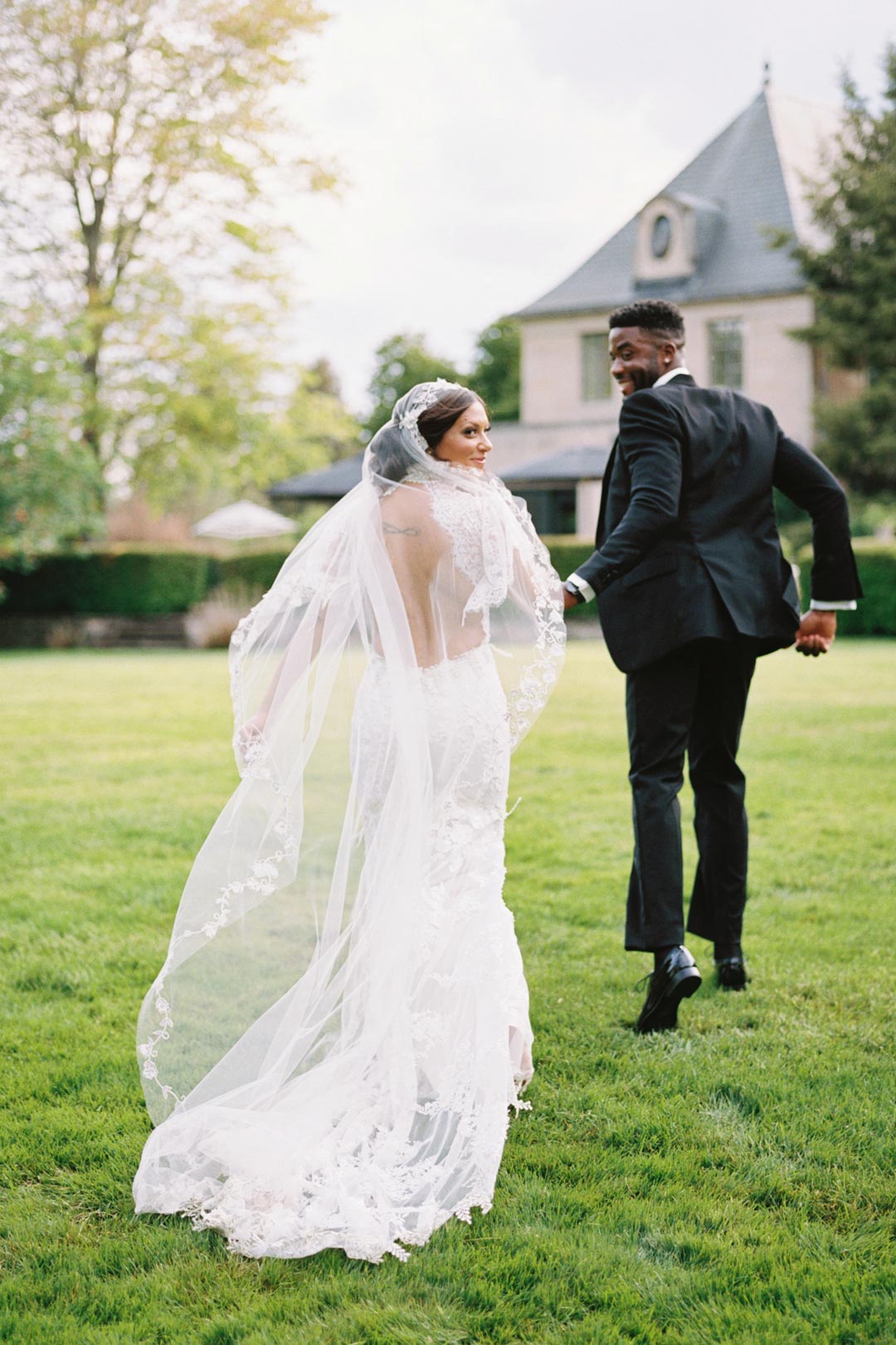 Bride in Grace Scoop Back Design Wedding Dress wear veil running on grass with Groom in Tux