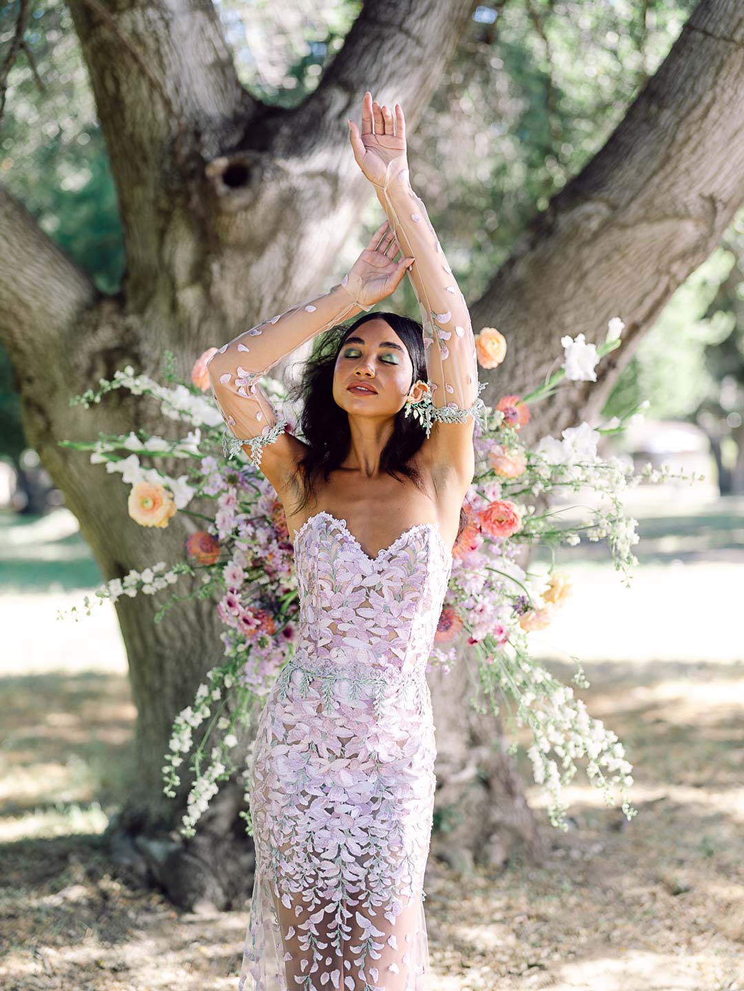 Bride wearing a strapless wedding gown with a sweetheart neckline and a fitted bodice, standing in front of a floral archway in a garden setting.