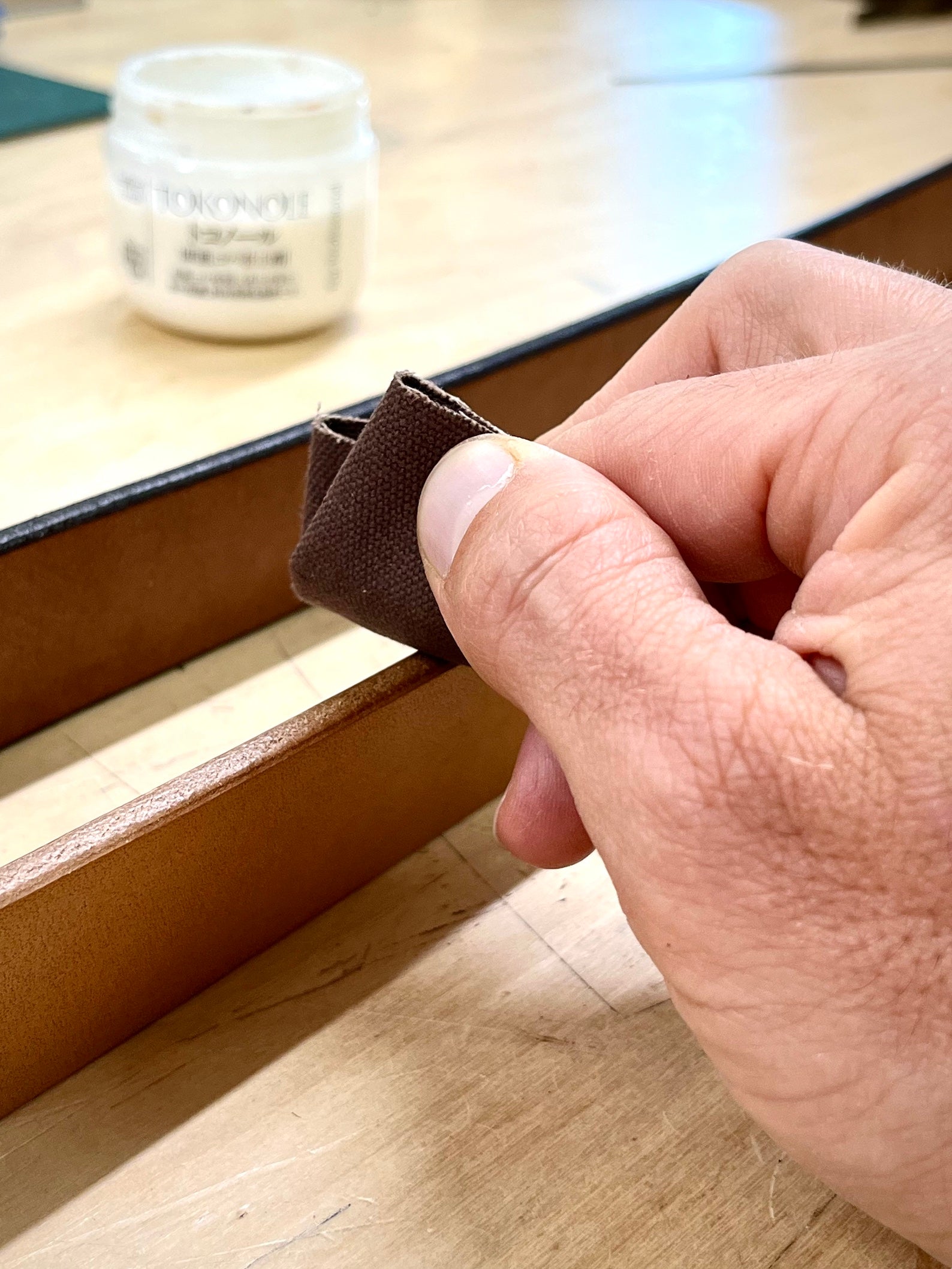 Hand burnishing a natural undyed oak bark leather belt with a clear edge finish and canvas cloth