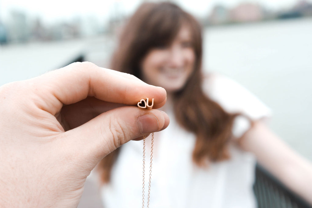 A woman stands while a necklace is held up in front of her