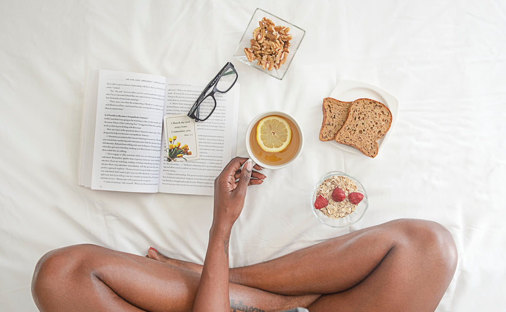 A girl has a book, coffee, glasses, and snacks in bed