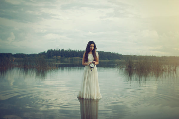 woman-in-dress-standing-in-water-holding-clock-against-abdomen