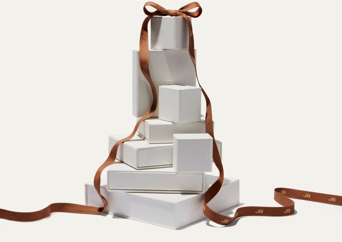 Stacked white gift boxes with a brown ribbon tied into a bow on top.