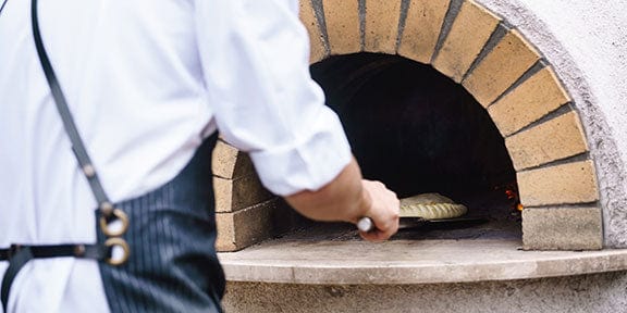 chef using an outdoor pizza oven