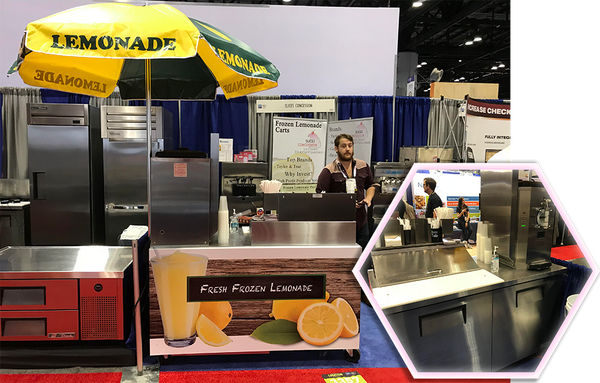 front part of frozen lemonade cart at a frozen desserts convetion with giant umbrella and frozen drink machine with small hexagon showing the inside and behind the counter part of the cart