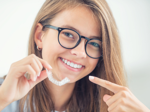 Happy person pointing to their pair of Invisalign braces over metal ones.