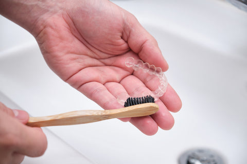 An image of someone brushing clear aligners to remove odor-causing bacteria.