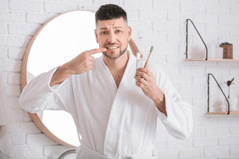 man in robe pointing to teeth toothbrush