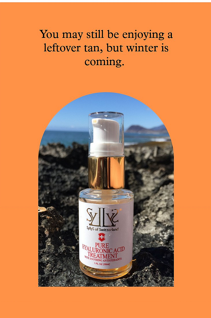 SyllyS Hyaluronic Acid with Soothing Antioxidants is in a glass clear pump bottle with gold rim and white label with gold logo and product’s titles printed in red below. It is on black reef with the ocean in the background. The image is placed in an arched orange frame that has a black text headline  “You may still be enjoying a summer tan, but winter is coming” 