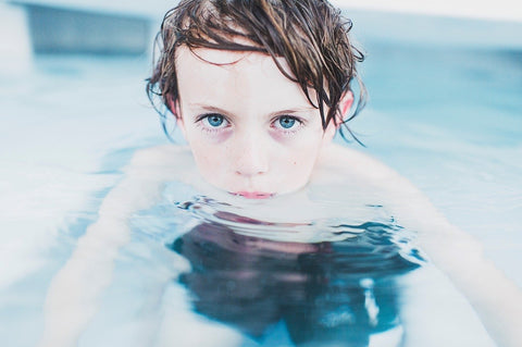 child with blue eyes in pool looking at the camera